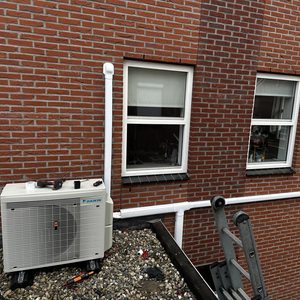 De afbeelding toont een geconfigureerde airconditioninginstallatie buiten een gebouw, met leidingen die naar binnen lopen.