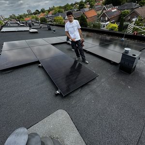 De afbeelding toont een installatie van zonnepanelen op het dak, met een technicus die bezig is met de installatie.