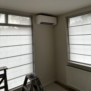 Een nieuwe airconditioning installatie hangt aan de muur in een kamer met verduisteringsgordijnen.