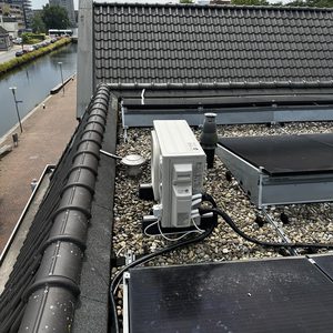 De afbeelding toont een airconditioning installatie op een dak, omringd door zonnepanelen en met een goed zicht op de omgeving.