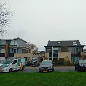 De foto toont een woning met zonnepanelen op het dak en enkele voertuigen geparkeerd op het erf.