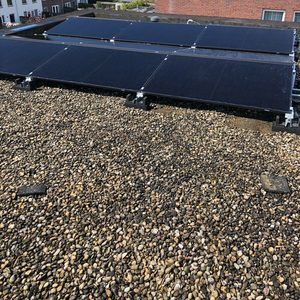 Zonnepanelen zijn geïnstalleerd op een plat dak van een woning, met een uitzicht op de omliggende huizen.