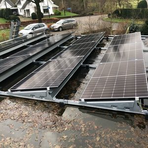 De afbeelding toont een installatie van zonnepanelen op een vlakke ondergrond, mogelijk een dak, met loeiende bladeren en water rondom.